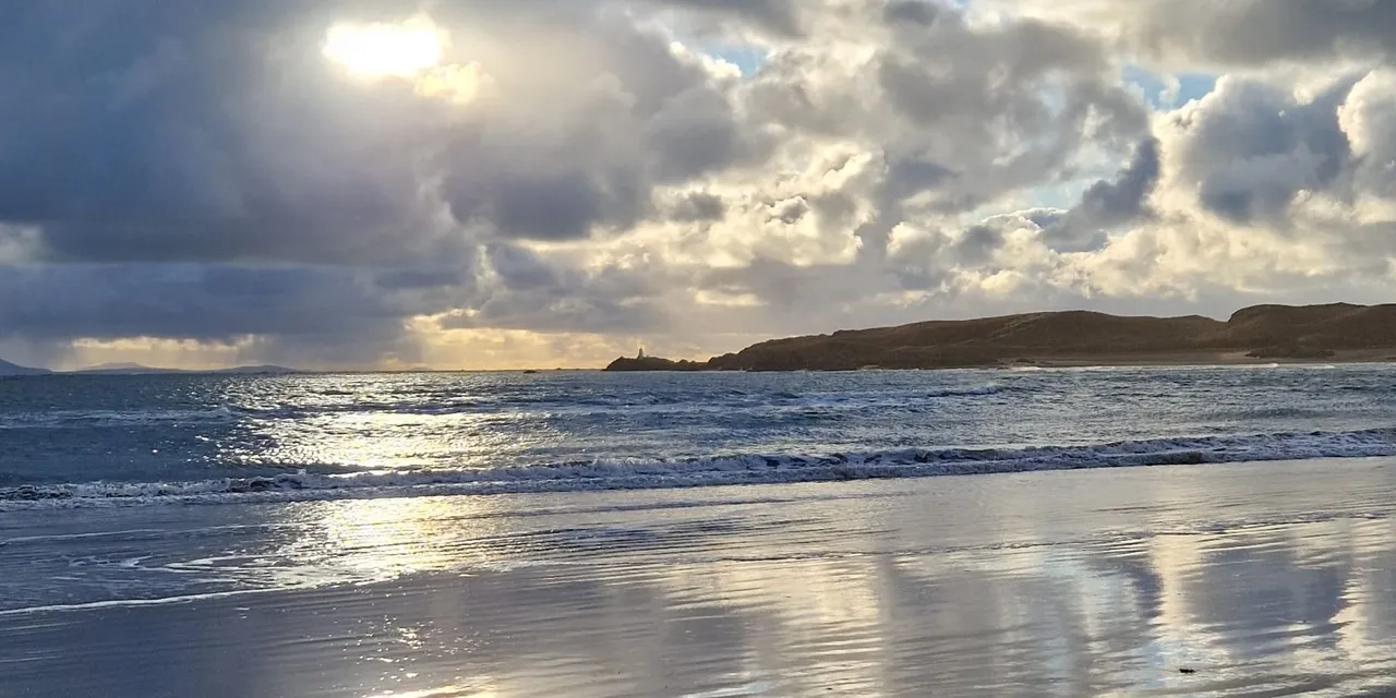 Low winter sun over Newborough beach, Anglesey, with cloud reflected in the wet sand and Ynys Llanddwyn on the horizon