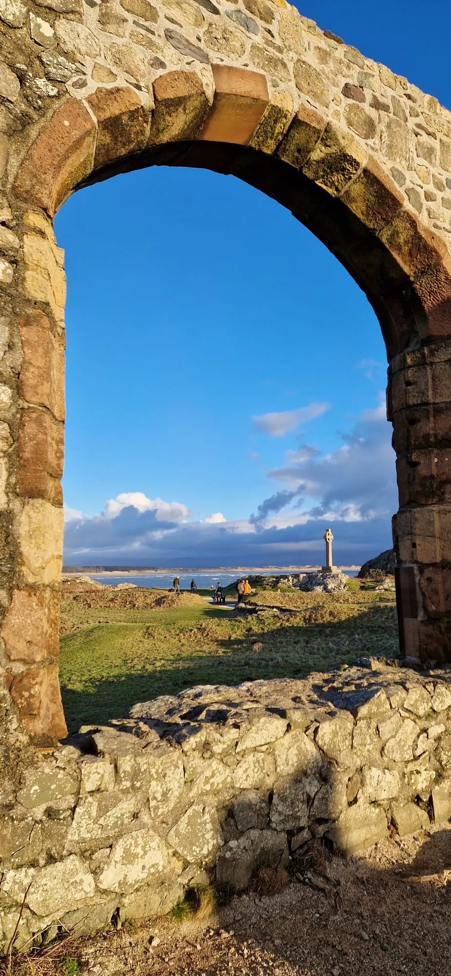 The surviving arch of St Dwynwen's chapel on Ynys Llanddwyn framing the Celtic cross and the sea beyond