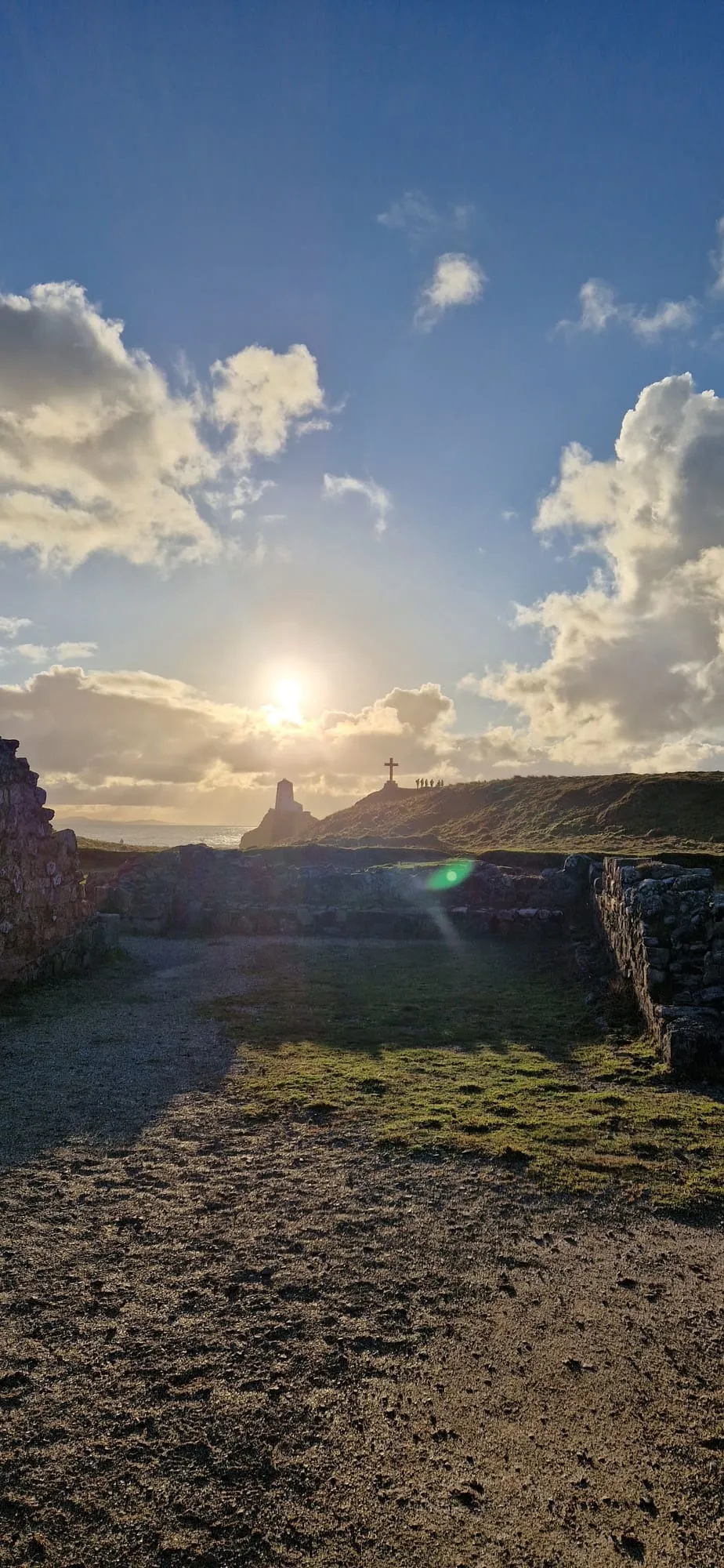 Inside the ruins of St Dwynwen's chapel, Ynys Llanddwyn, looking out to the cross and Tŵr Bach lighthouse against a low sun